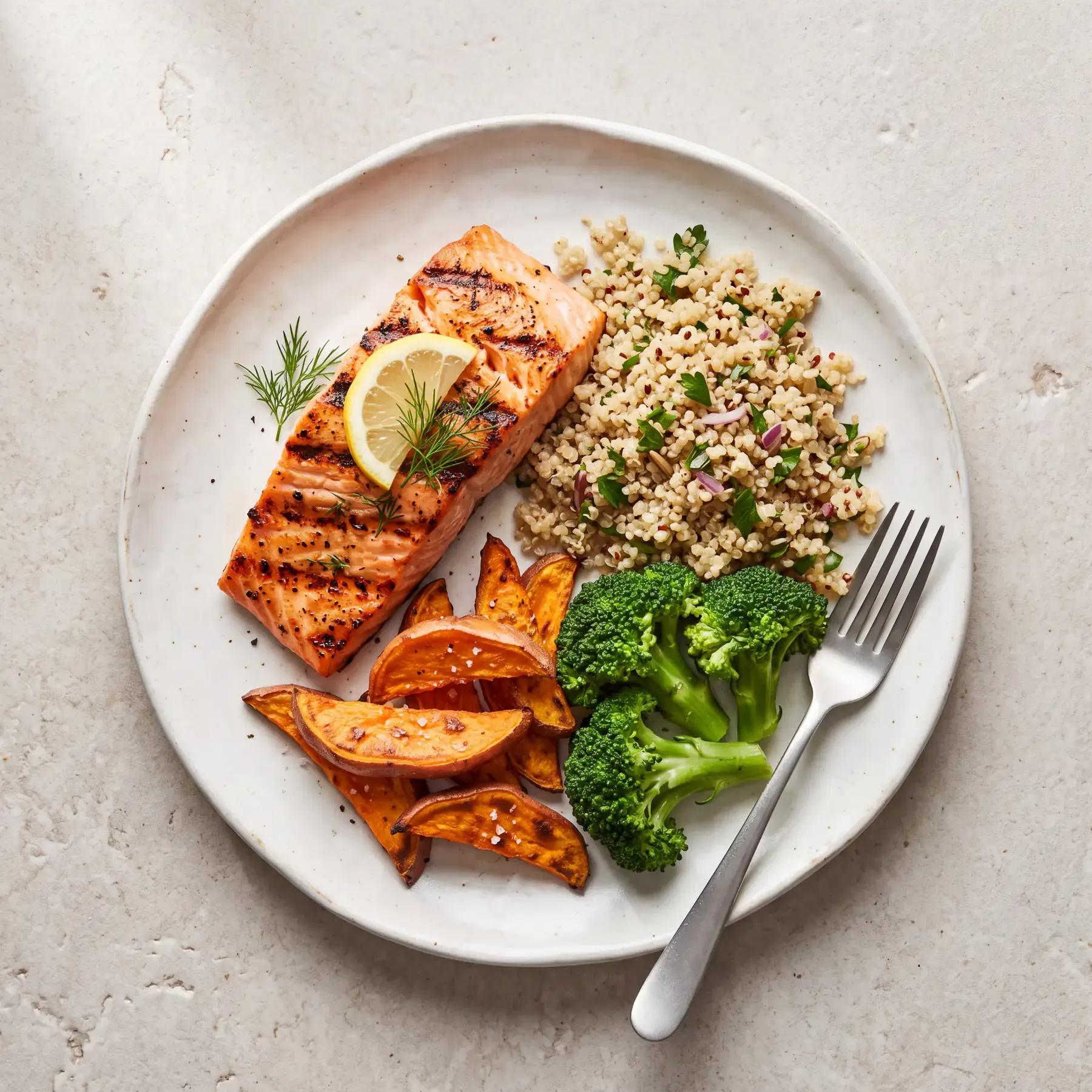 A meal of grilled salmon, quinoa, roasted sweet potato, and steamed broccoli photographed from above